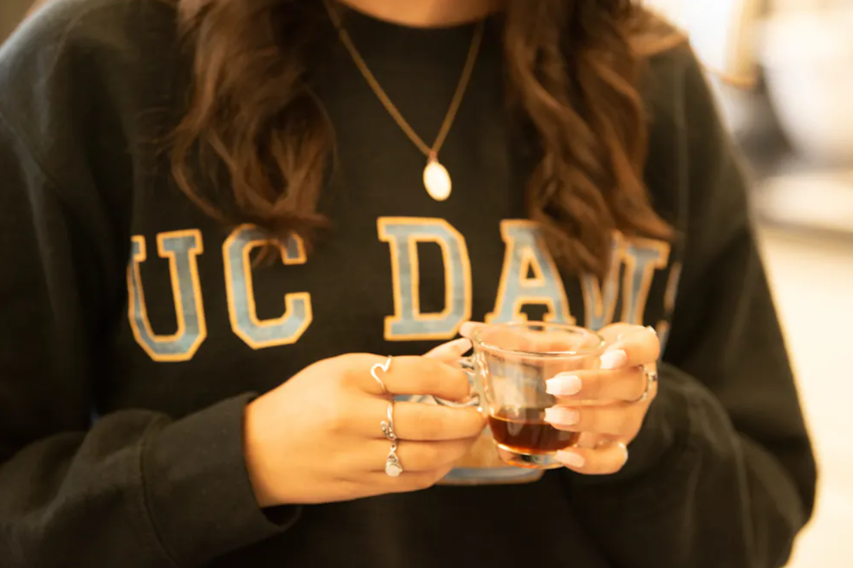 Close up of hands holding a coffee cup and a UC Davis sweatshirt
