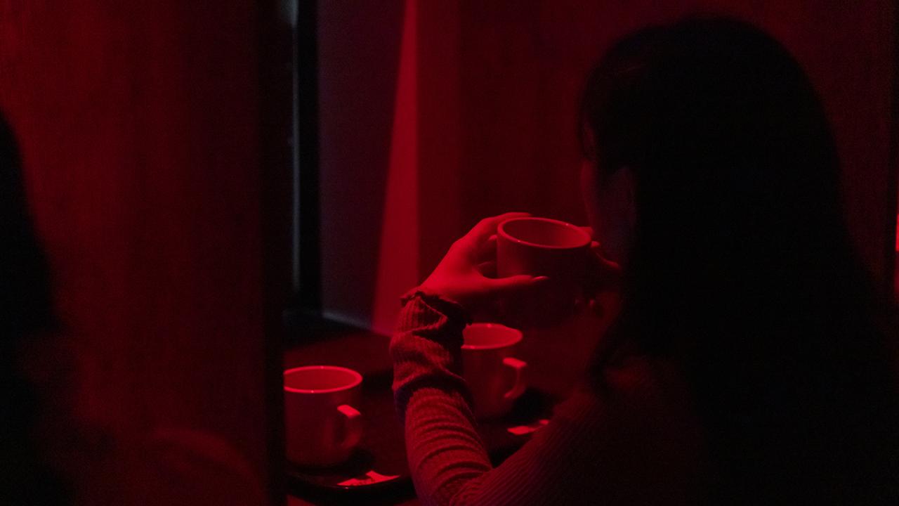 Someone sips coffee in a red lit room