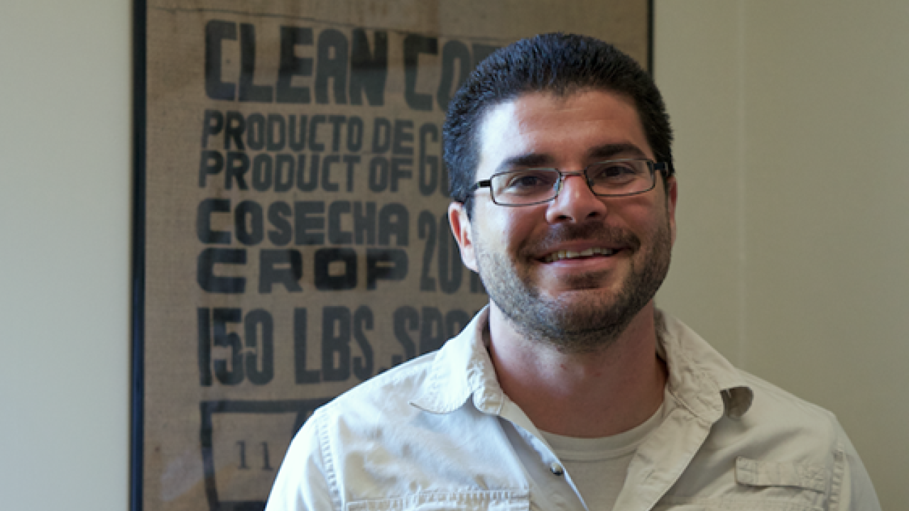 Irwin Donis-González standing indoors next to a framed coffee bag